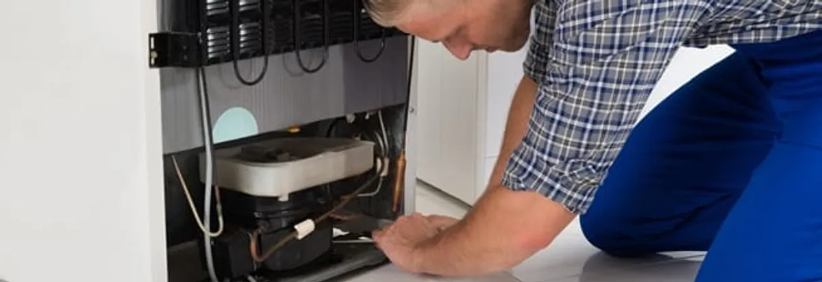 Refrigerator repair technician servicing the compressor and condenser area in Oklahoma City, OK